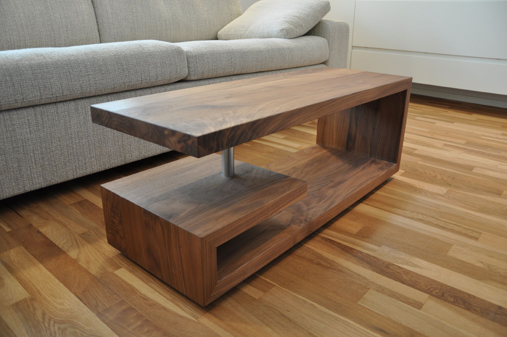 Modern geformter Couchtisch aus massivem Nussbaumholz und dem Edelstahlzylinder als stabilisierende Verbindung zwischen Tischplatte und  Unterbau.